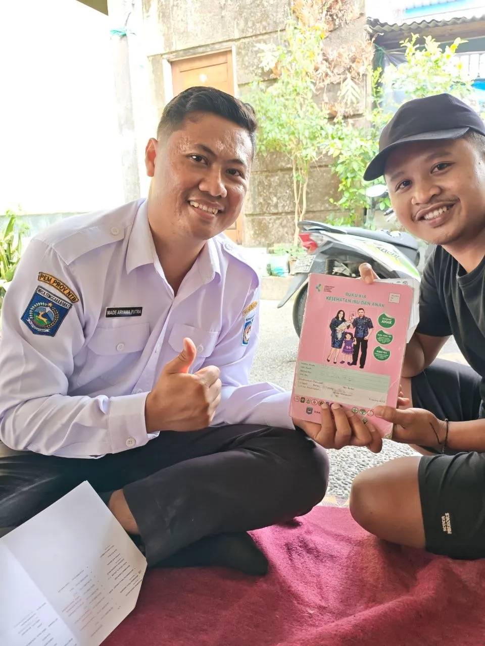 Petugas dan seorang ayah menunjukkan buku KIA sambil tersenyum