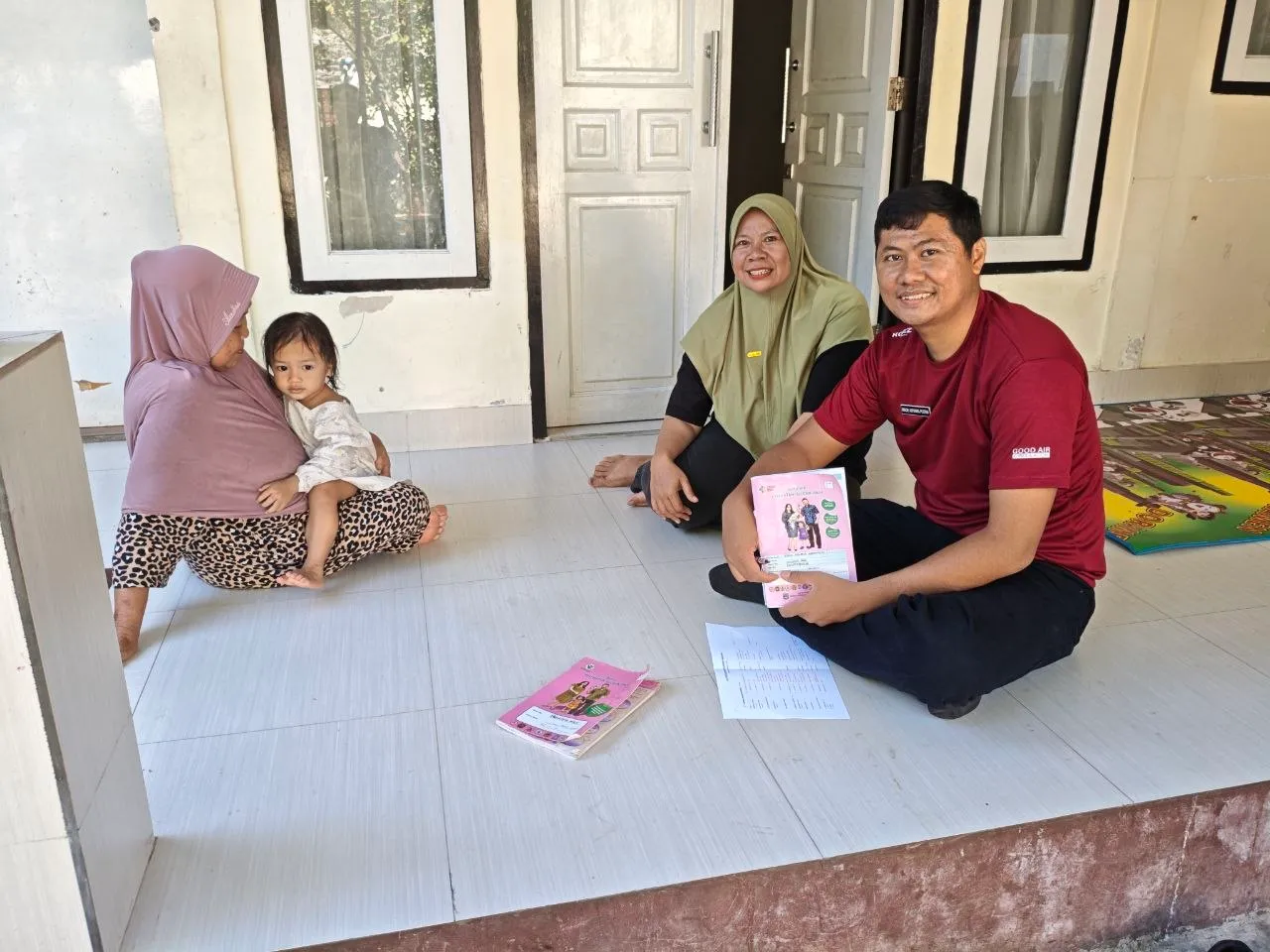 Petugas duduk bersama ibu dan anaknya, membahas buku KIA