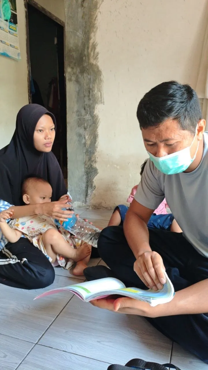 Petugas membacakan buku kepada seorang ibu yang memangku bayinya