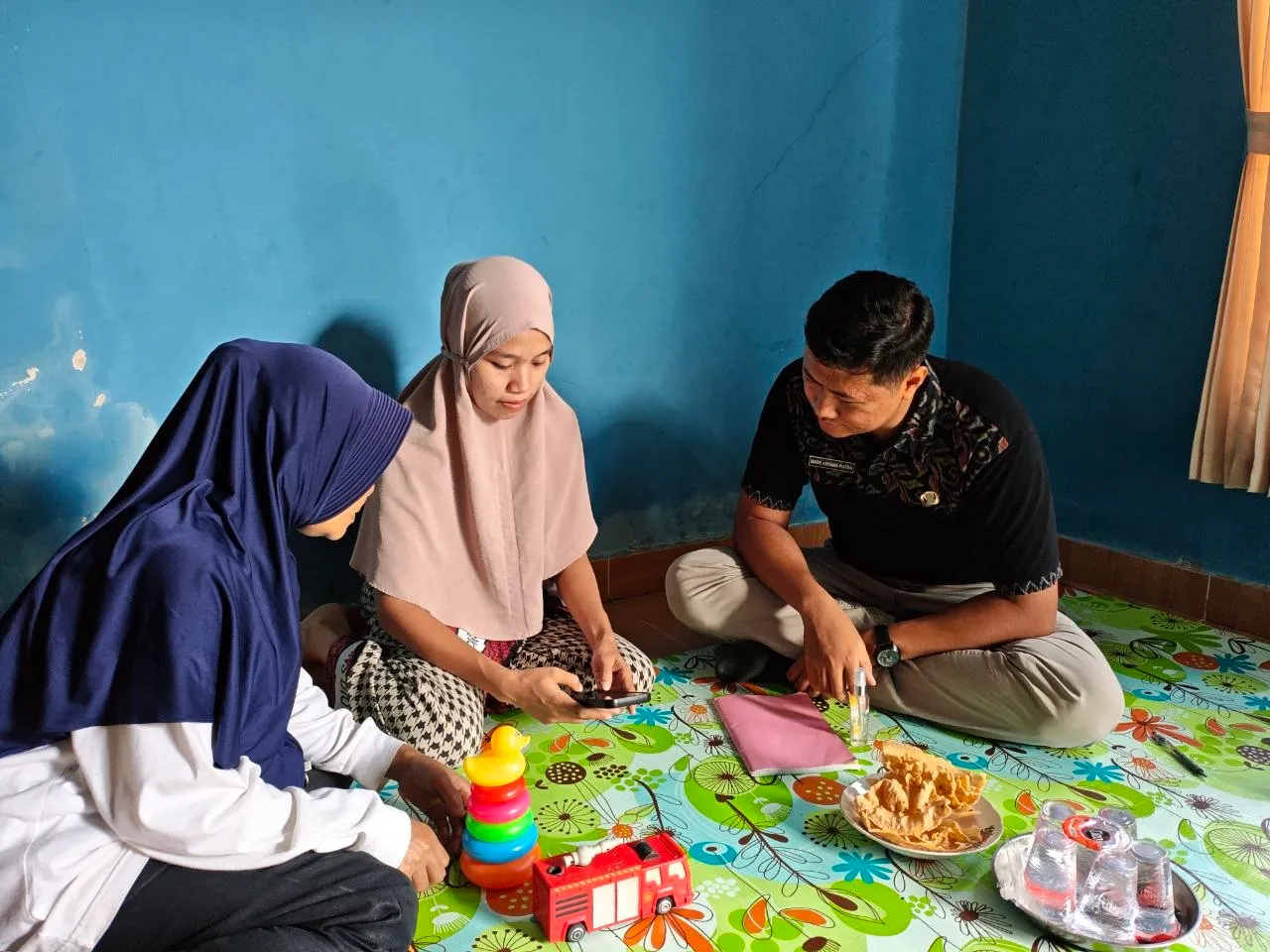 Petugas berbincang dengan dua orang ibu di atas tikar bermain anak